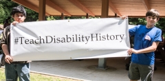 Ben (r) and friend hold the Teach Disability History campaign banner