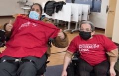 Colleen and another woman, both in wheelchairs, with BCIL shirts indoors