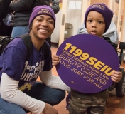 Young boy and his mom, holding an 1199SEIU sign, indoors
