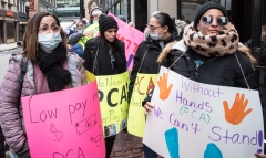 women with signs "Low Pay makes PCA Shortages" and "Without Hands (PCAs), we can't stand"