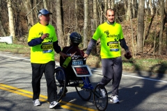 Bill Reilly in wheelchair facing backwards with two guides