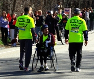 Bill Reilly in wheelchair facing backwards with two guides