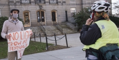 Advocate with Sign "No Light Show at Fernald" educates woman on her bike.