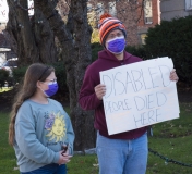 Man and daughter.  Sign: "disabled people died here"