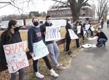 Students stand along fence with signs