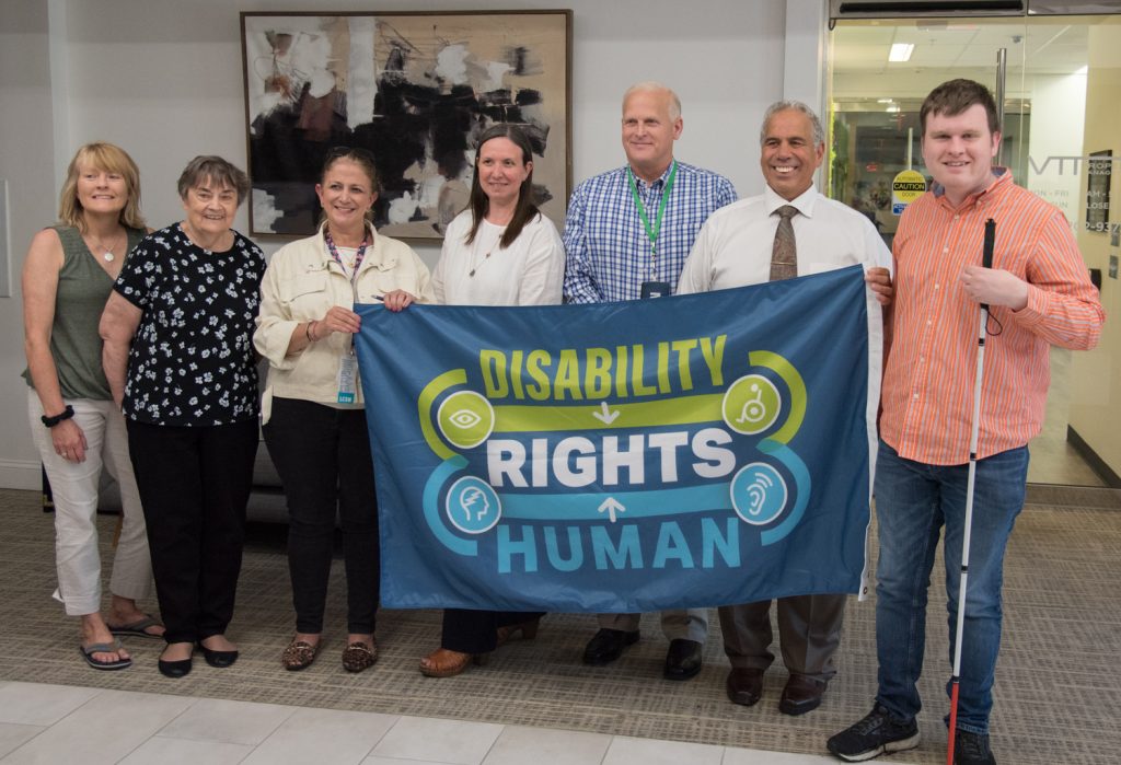 Staff and community members hold flag saying disability rights human rights. This flag will be flown at Framingham City Hall