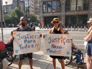Man and woman with signs saying Justica Para Todos (Justice for Everyone)