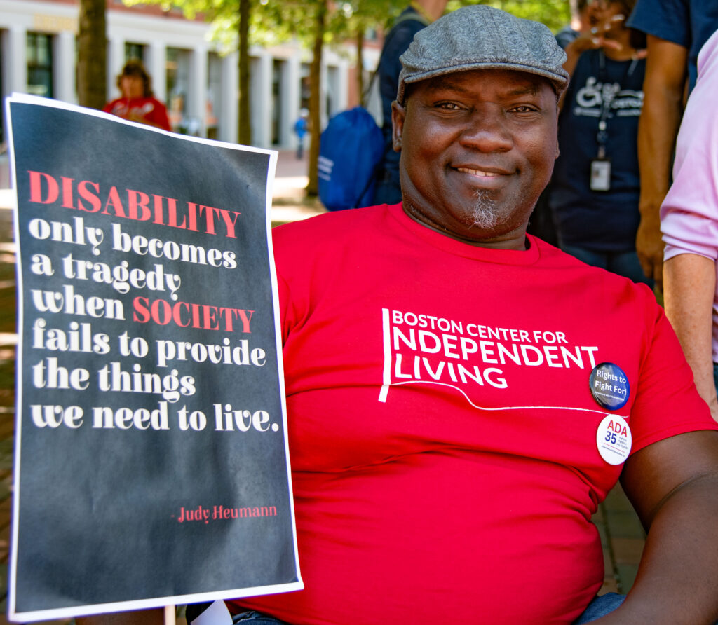 Murshid of BCIL with sign: Disability only becomes a tragedy when society fails to provide the things we need to live