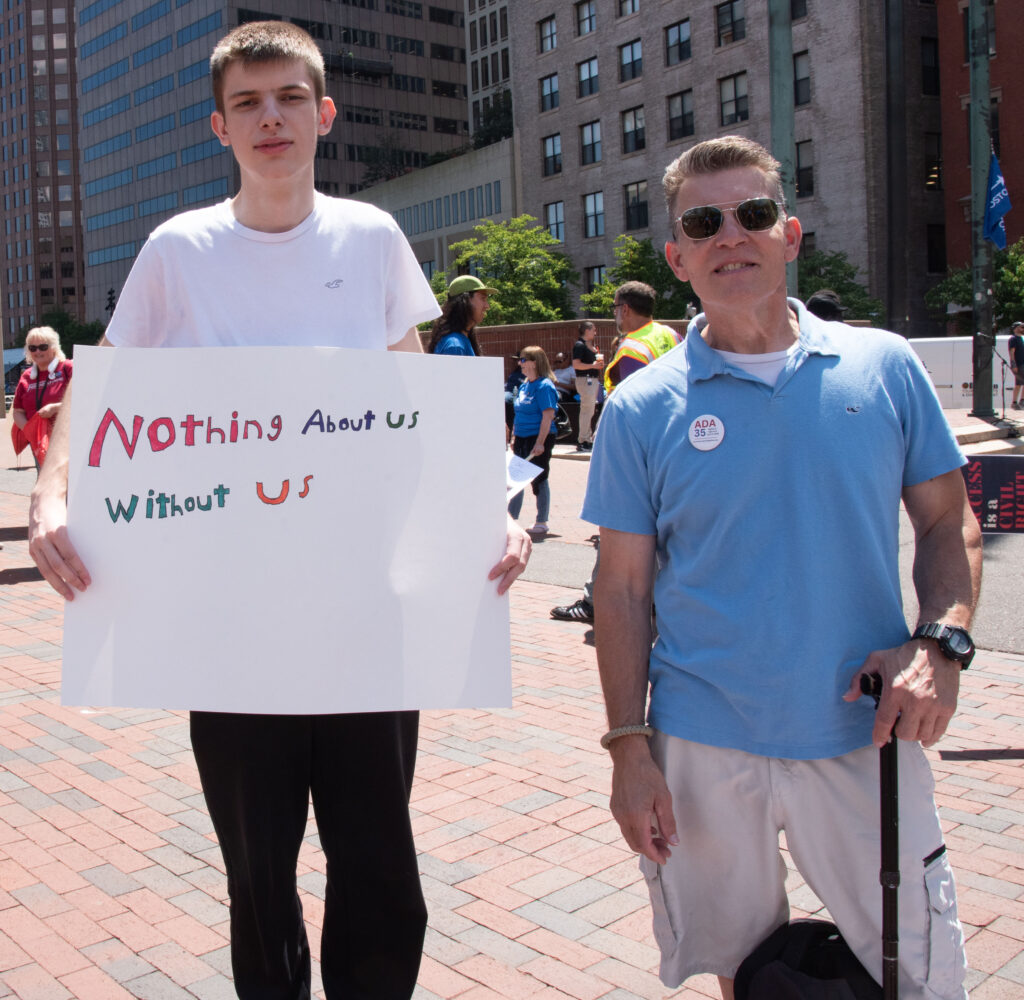 MWCIL - two men. Sign "Nothing about us without us"