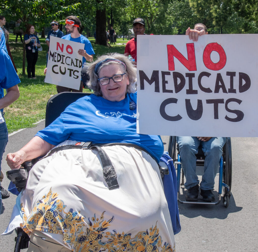 woman in chair with sign: No Medicaid Cuts