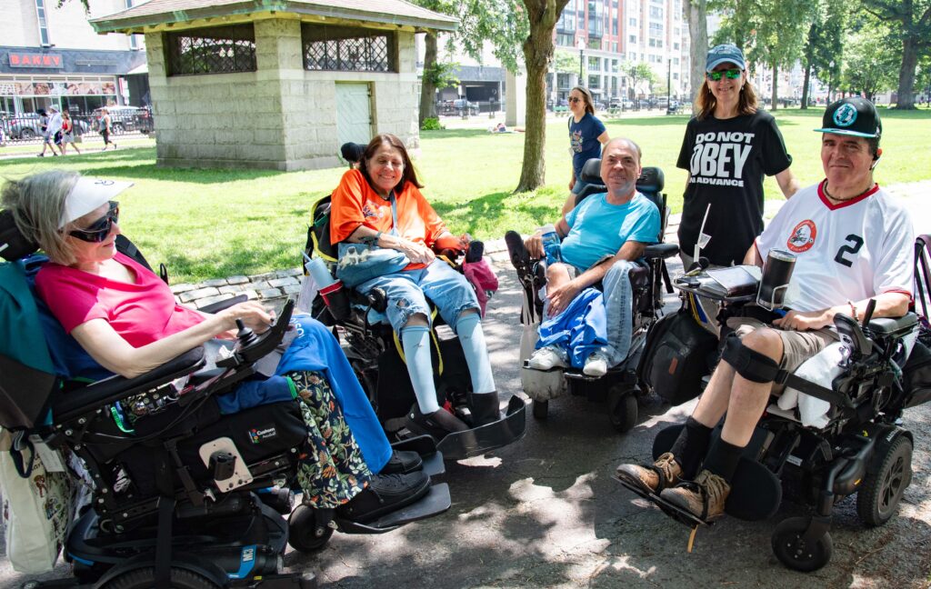 4 people in wheelchairs talking to a 5th person
